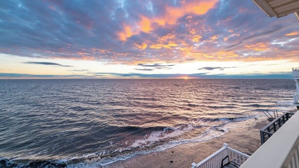 Une vue sur la côte, avec un coucher de soleil, des vagues de l’océan et un bâtiment doté d’un balcon.