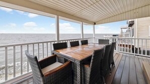 Une terrasse extérieure couverte, dotée d’une table en bois et de chaises en osier, avec vue sur la mer.