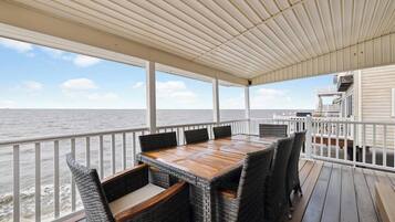En overdækket terrasse med et træbord og fletstole, med udsigt over havet.