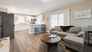 Un salon moderne avec un canapé, une table basse et un coin cuisine doté de meubles blancs et d’un îlot central.