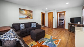 A living room with a sofa, ottoman, starfish rug, and a painting on the wall.