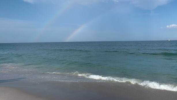 A beach with a visible rainbow over the ocean.
