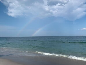 A beach with a visible rainbow over the ocean.