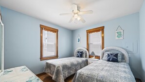 A bedroom with two single beds, a ceiling fan, and a window with blinds.