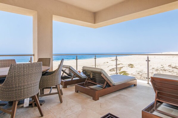 A beachside patio with lounge chairs, a table, and a view of the ocean.