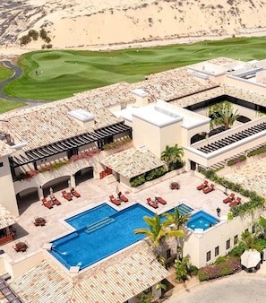 A resort with a swimming pool, outdoor seating, and a golf course in the background.
