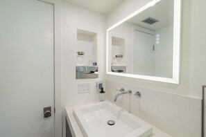 A modern bathroom with a white sink, a large mirror, and a wall-mounted soap dispenser. - Village Camp Truckee (Truckee)