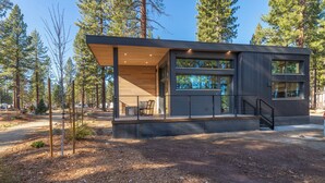 A modern cabin with a large deck, surrounded by tall pine trees. - Village Camp Truckee (Truckee)