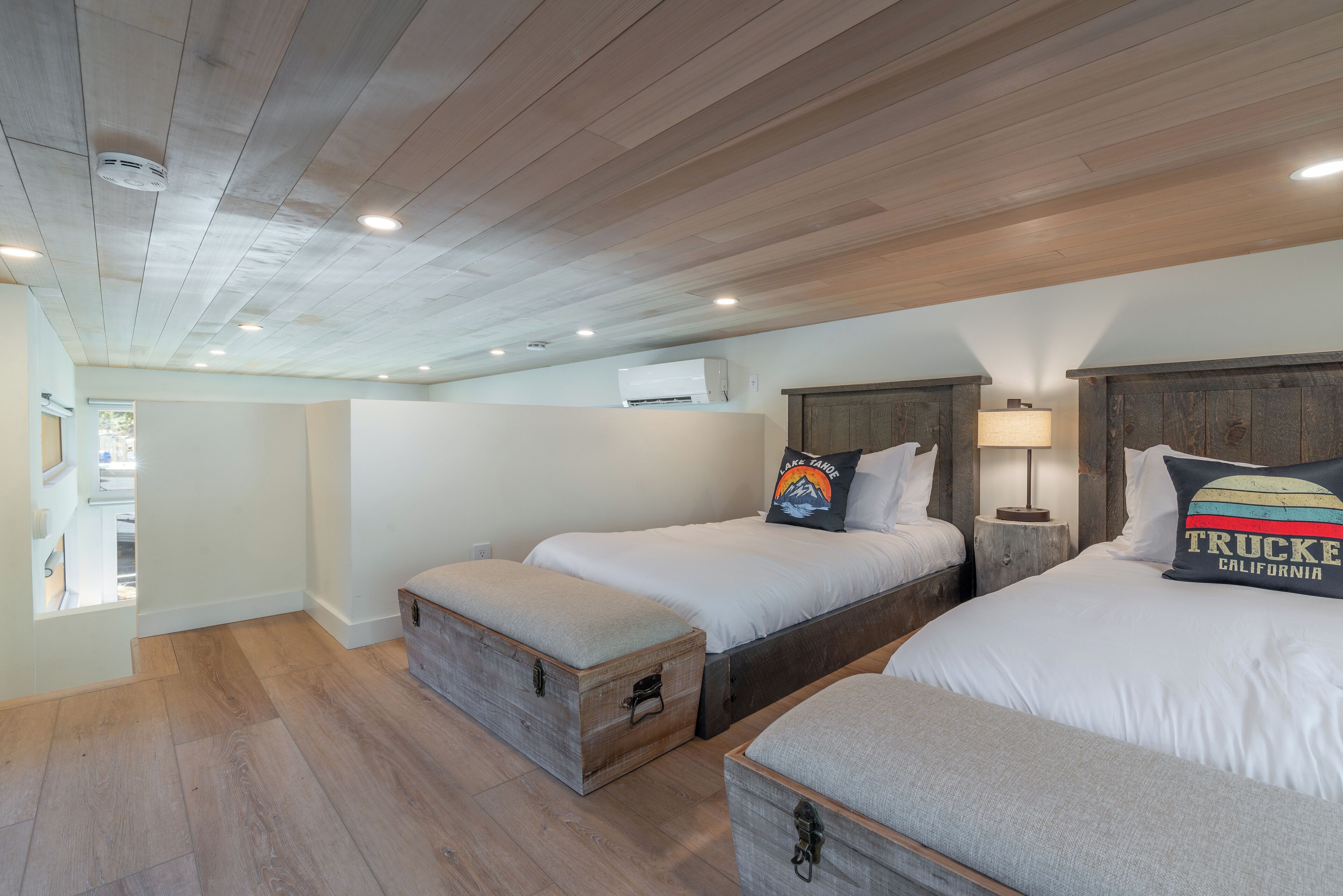 A bedroom with two beds, wooden headboards, and a small bedside table with a lamp.