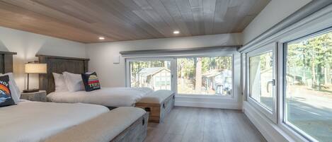Une chambre avec deux lits, une tête de lit en bois, de grandes fenêtres et une vue sur l’extérieur.