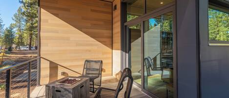 A modern outdoor deck with wooden flooring, metal chairs, and a built-in fire pit.