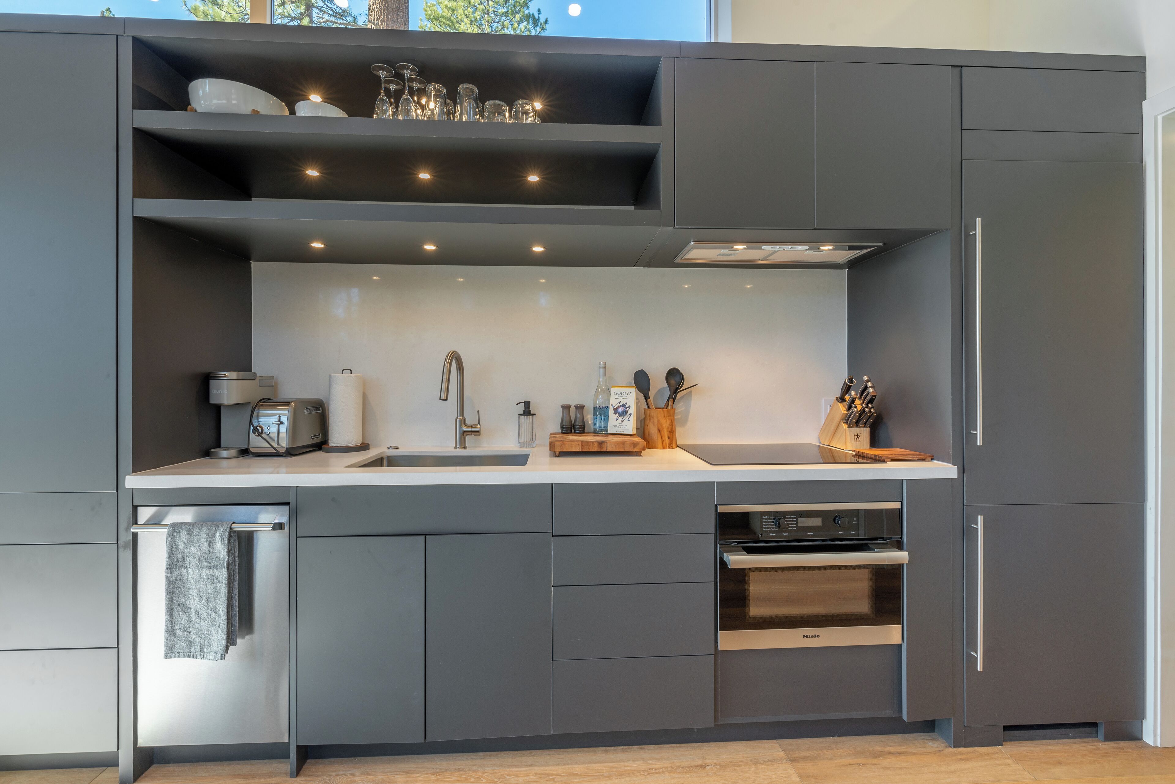 Een moderne keuken met grijze kastjes, een inbouwoven, een spoelbak en een afwasschaal.