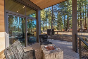 A modern outdoor deck with wicker furniture, a stone table with snacks, and a glass door leading to an interior space.