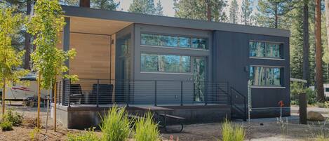 A modern cabin with large windows, a covered deck, and a natural forest backdrop.