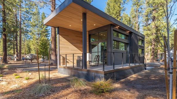 A modern cabin with a wooden deck, large windows, and a view of the surrounding forest. - Village Camp Truckee (Truckee)