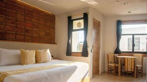 A bedroom with a bed, a small table with chairs, a window with curtains, and a brick wall.