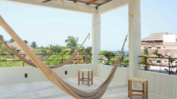 A balcony with a hammock, two wooden stools, and a ceiling fan.