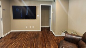 A spacious room with a large flat-screen TV mounted on the wall, wooden flooring, and a leather recliner.