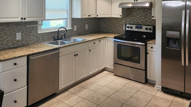 A modern kitchen with white cabinets, a stainless steel refrigerator, a built-in oven, and a granite countertop.