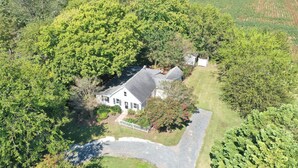 An aerial view of a house surrounded by dense greenery, with a driveway leading to the front door.