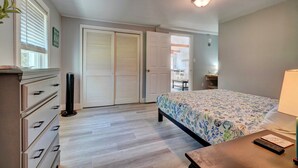 A bedroom with a bed, dresser, bedside table, lamp, and a view of a hallway with a door.