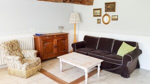 Una sala de estar con un sillón estampado, un sofá marrón oscuro con una manta verde, un aparador de madera y una mesa de centro blanca.