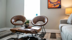 En stue med to læderstole, et træbord, en lille plante, et billede på væggen og en sofa.