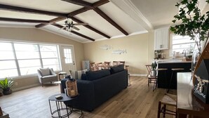 Ein geräumiger Wohnbereich mit einem dunkelgrauen Sofa, Holzboden und Deckenventilator.