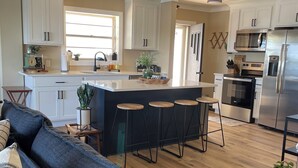 Eine moderne Küche mit weißen Schränken, einer zentralen Kochinsel mit Barhocker, einem eingebauten Ofen und einem Kühlschrank.