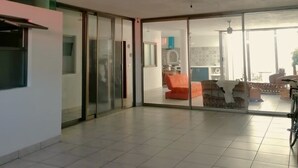 A spacious room with a tiled floor, a sliding glass door leading to a living area with a sofa and a bicycle, and a kitchen area with a stove and cabinets.