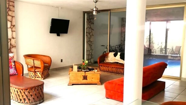 A spacious living area with a sofa, chairs, a coffee table, and a TV mounted on the wall.