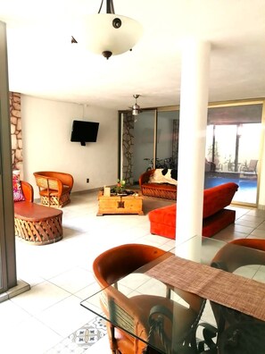 Un amplio salón con sofá, sillones, una mesa de centro y un televisor montado en la pared.