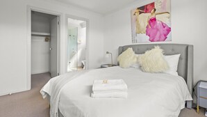 Quarto moderno com cama grande, mesa de cabeceira, espelho e um quadro na parede.