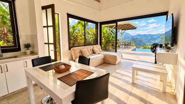 A modern kitchen with a dining area, a sofa, and a view of mountains.