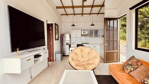 Un salon moderne avec un téléviseur à écran plat, une table basse blanche, un canapé orange, un fauteuil à capitonnage et un ventilateur de plafond.