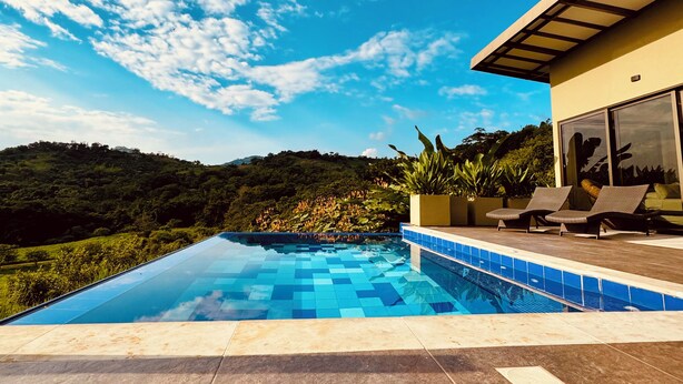 Une piscine extérieure moderne, avec un ciel bleu dégagé et un paysage vallonné en arrière-plan.