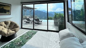 Une chambre avec un lit, un ventilateur de plafond, une grande fenêtre et une vue sur une piscine et des montagnes.
