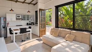 A modern kitchen with a dining area and a large window with a view of greenery.