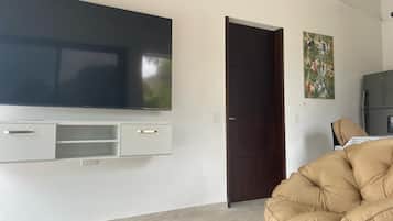A modern living room with a flat-screen TV mounted on the wall, a dark wooden door, and a beige armchair.