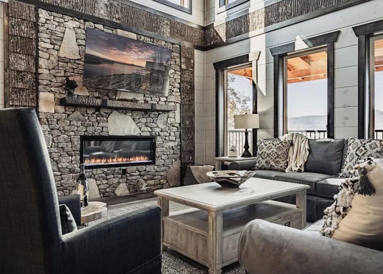 A living room with a stone fireplace, a sofa, a coffee table, and a large window.