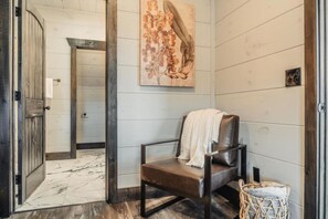 A room with a wooden door, a bench with a white towel, a woven basket, and a painting on the wall. - Fully Loaded l Heated Pool l Game Room l Hot Tub (Sevierville)