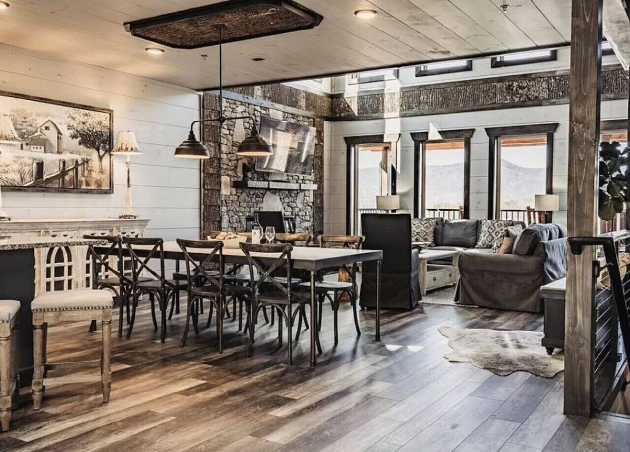 A rustic interior with a dining area, sofa, and large windows.