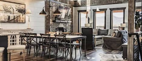 A rustic interior with a dining area, sofa, and large windows.