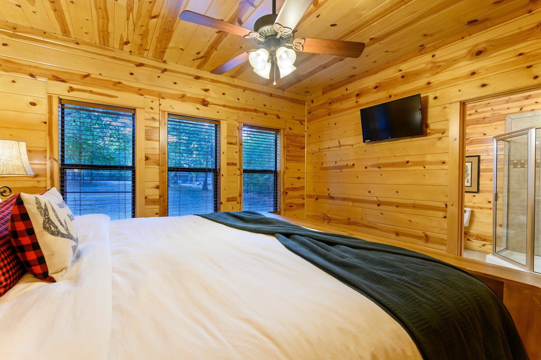 Un dormitorio de cabaña de madera con una cama, un ventilador de techo y un televisor montado en la pared.