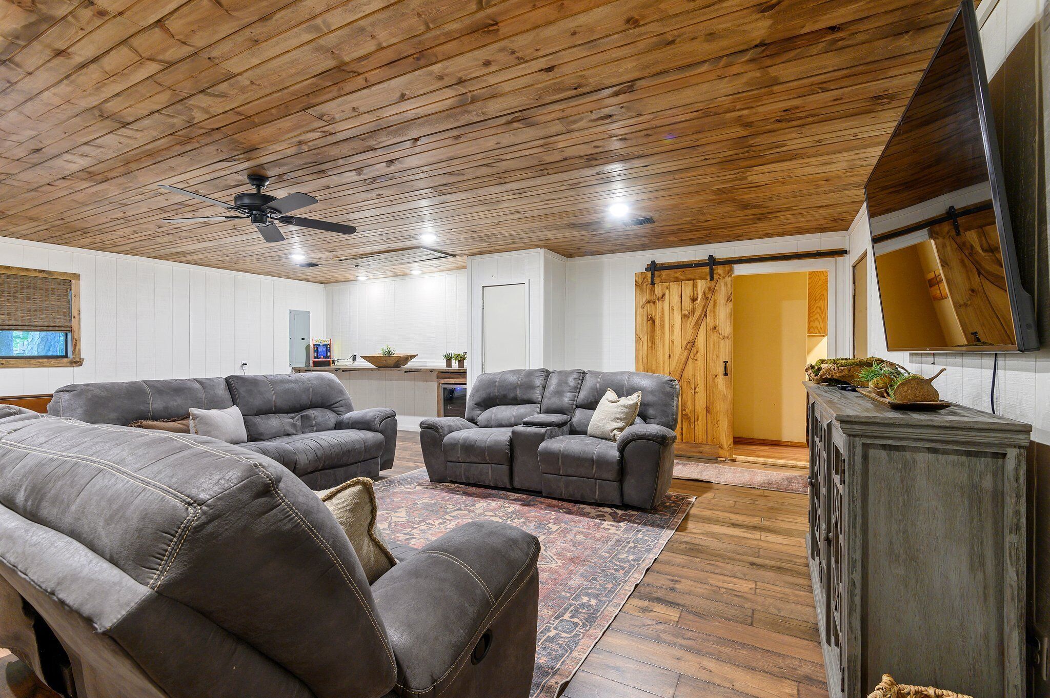 A spacious living room with a wooden ceiling, two grey sofas, a coffee table, and a wooden cabinet.
