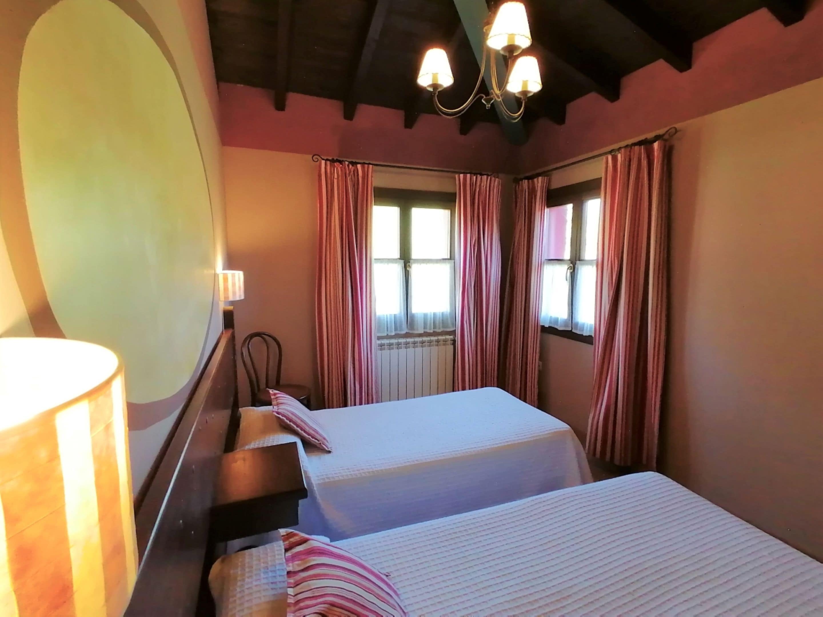 Una habitación con dos camas, una silla, una ventana con cortinas y un candelabro.