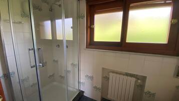 A bathroom with a glass shower enclosure, a toilet, and a window above the sink.