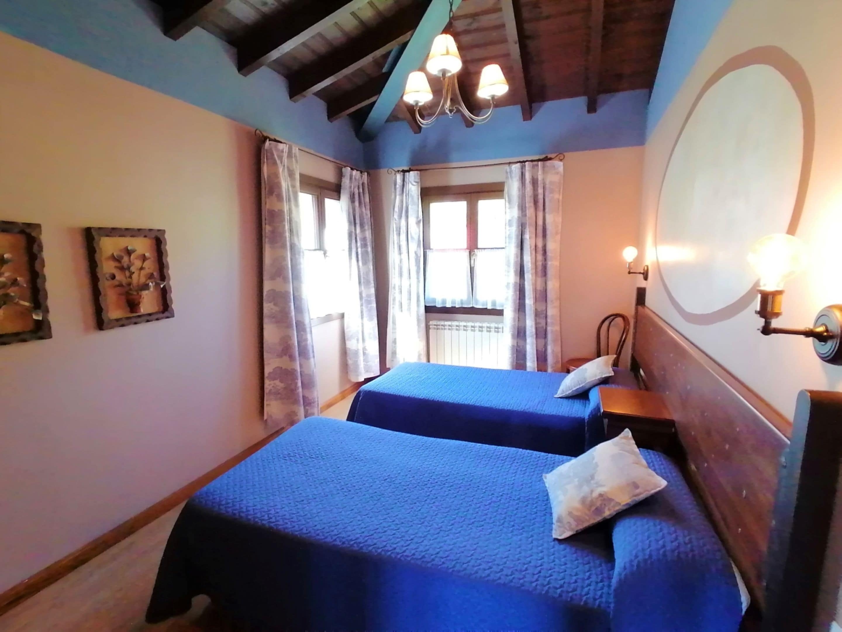 Une chambre avec deux lits, un plafond en bois, une fenêtre avec des rideaux et un luminaire fixé au mur.