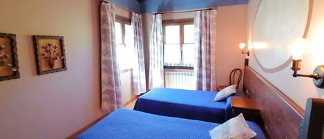 Une chambre avec deux lits, un plafond en bois, une fenêtre avec des rideaux et un luminaire fixé au mur.