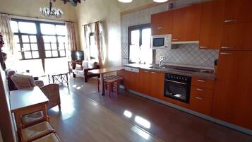 A spacious kitchen with wooden cabinets, a dining area with wicker chairs, and a television in the living room.